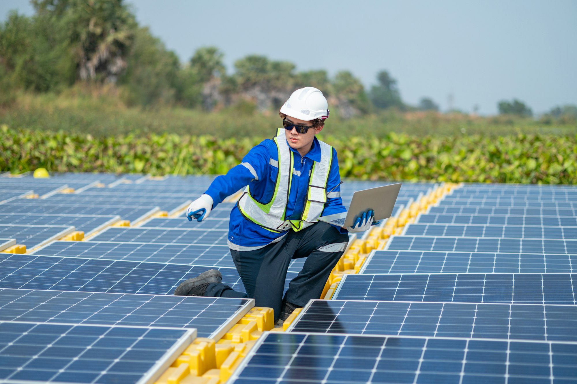 Un tehnician solar în echipament de siguranță folosește un laptop pentru a monitoriza și analiza performanța panourilor solare într-o zi însorită.