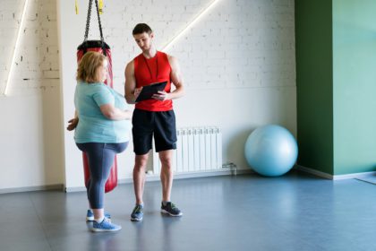 Portret pe toată lungimea unui instructor de fitness frumos care vorbește cu o femeie obeză în timpul antrenamentului personal în sală, spațiu de copiere